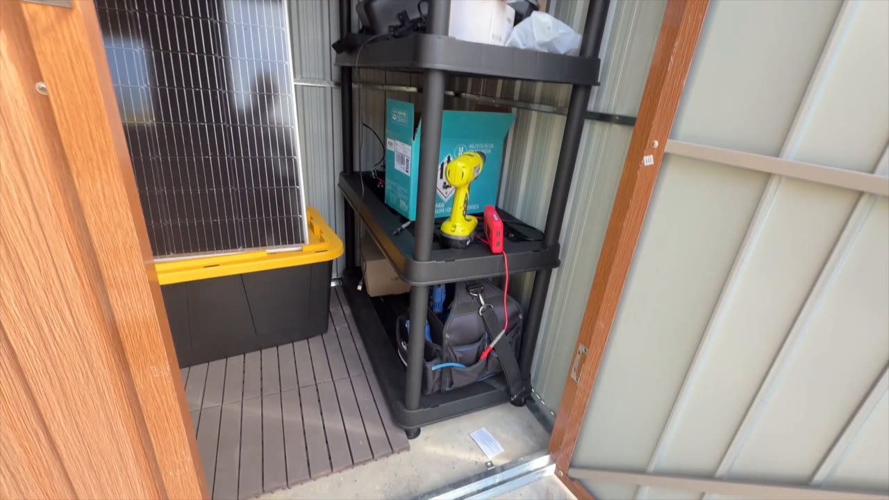 Florise 6x4 metal storage shed with the door open, showing a storage rack holding tools and electronics on a deck tile floor