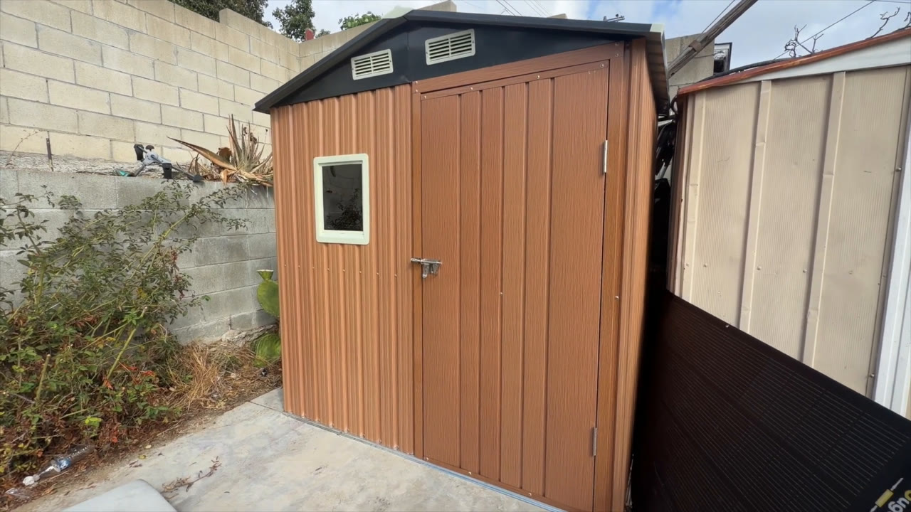 Front view of the Florise 6x4 metal storage shed in a backyard with wood-look panels, window, door latch and gable vents